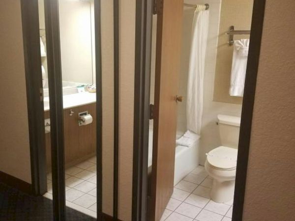 A hotel room hallway with a mirrored closet, open doorway to a bathroom showing a shower, toilet, and sink.