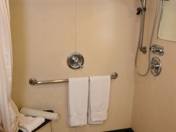 A tiled shower room with a handheld shower, wall-mounted controls, a curved curtain rod, and two white towels hanging on a bar.